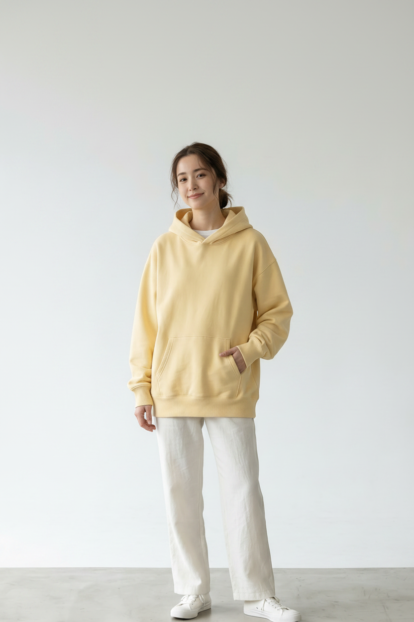 Butter yellow pullover hoodie side view — relaxed-fit fleece hoodie in a soft cream/butter yellow with a structured oversized hood, kangaroo pocket, and ribbed cuffs and hem. Shown from the left side profile against a white background.